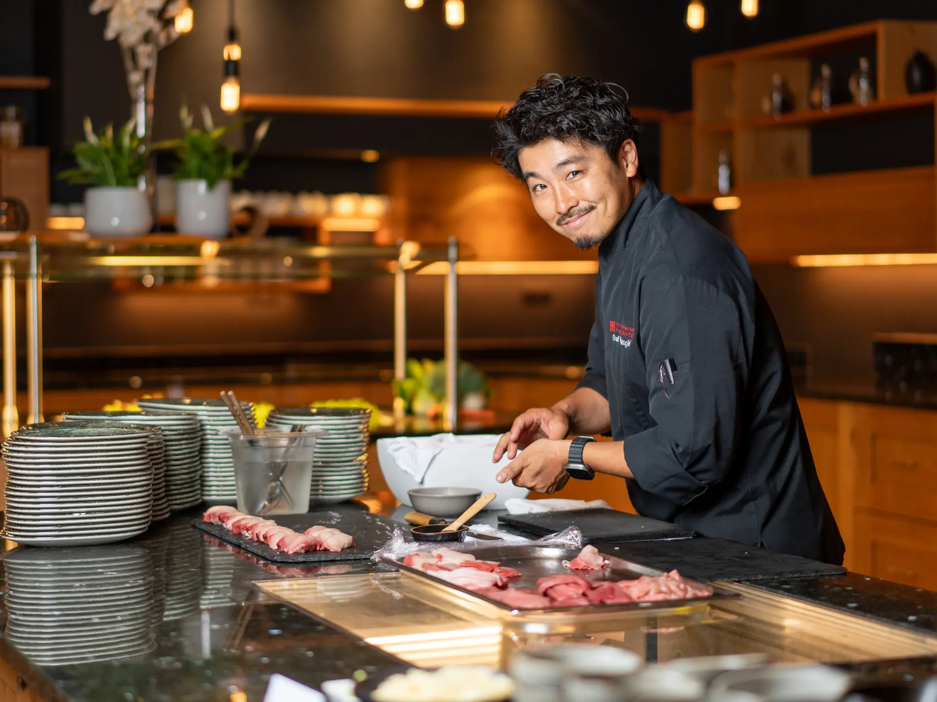 Lächelnder asiatischer Koch bei Sushi-Zubereitung an Theke | © johannes brunner