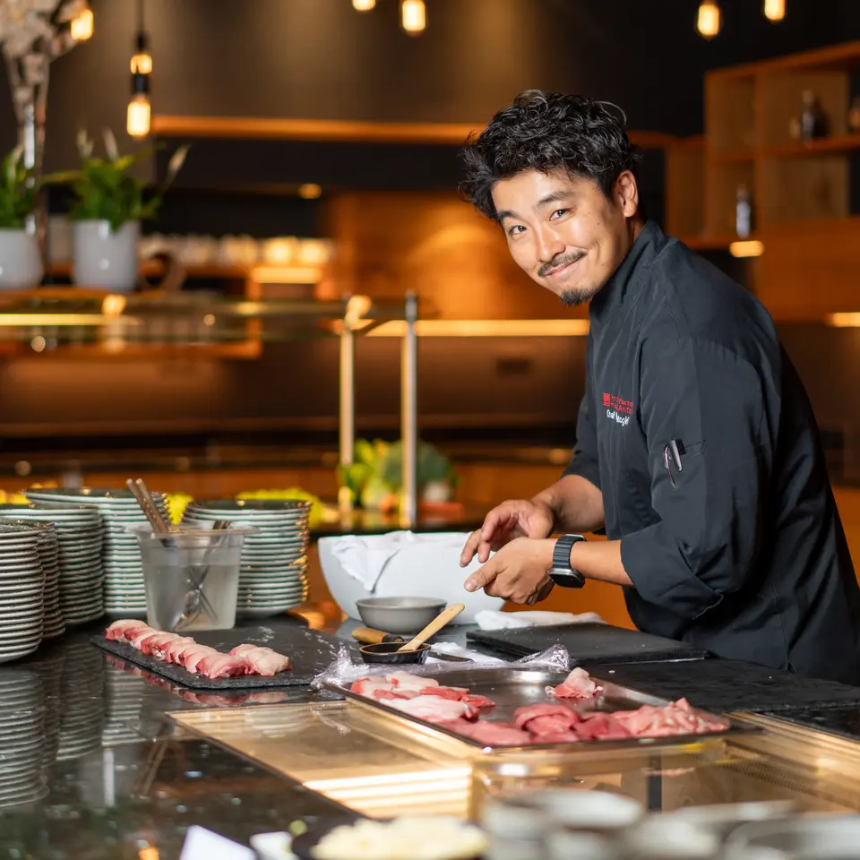 Lächelnder asiatischer Koch bei Sushi-Zubereitung an Theke | © johannes brunner
